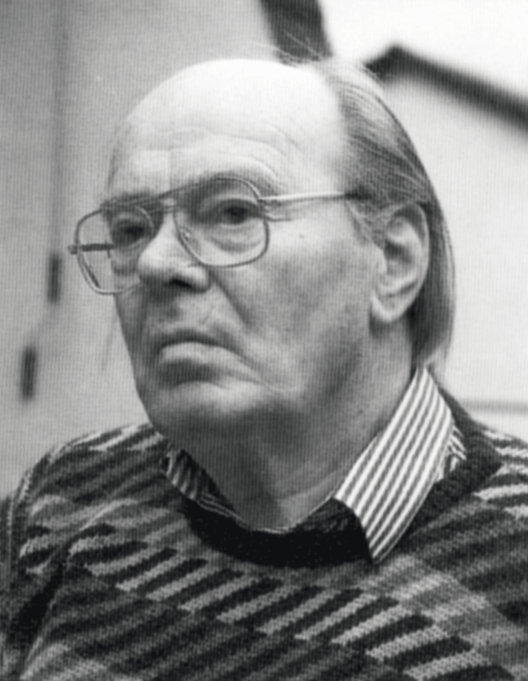 Porträt eines älteren Mannes mit Brille und kurzen Haaren, bekleidet mit einem gestreiften Pullover.